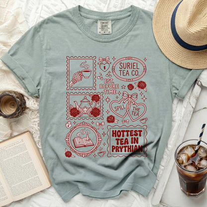 Green t-shirt with red graphic featuring stamps: skeleton hand holding tea, teapot, book with candle, and text.