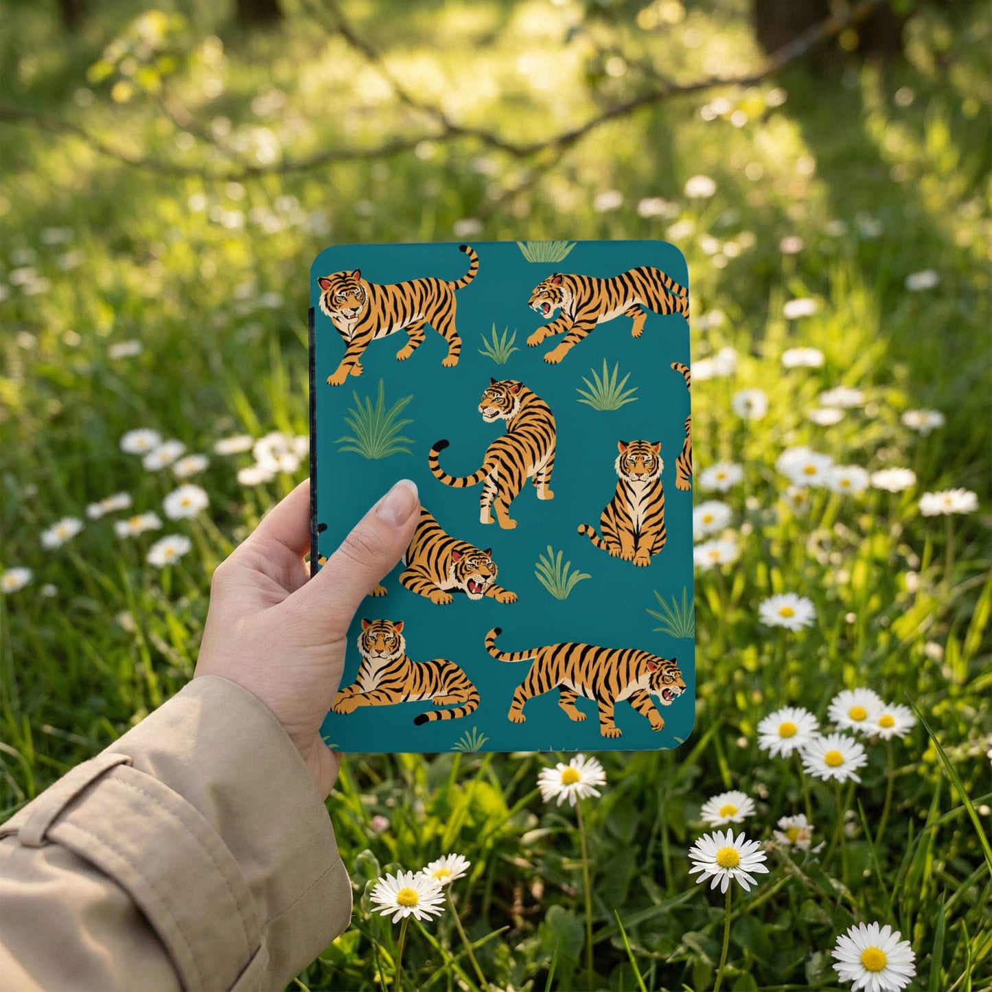 Teal case with tiger pattern held in hand against a backdrop of green grass and white daisies.