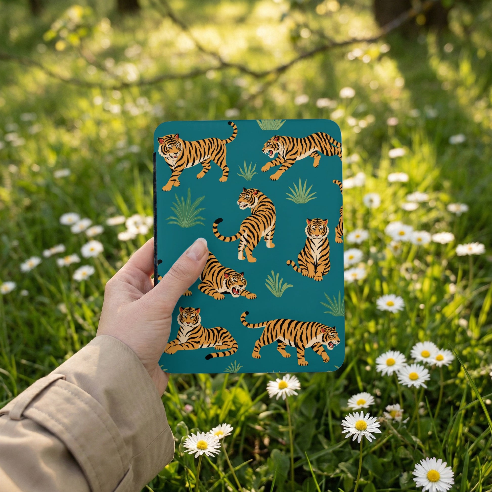 Teal case with tiger pattern held in hand against a backdrop of green grass and white daisies.