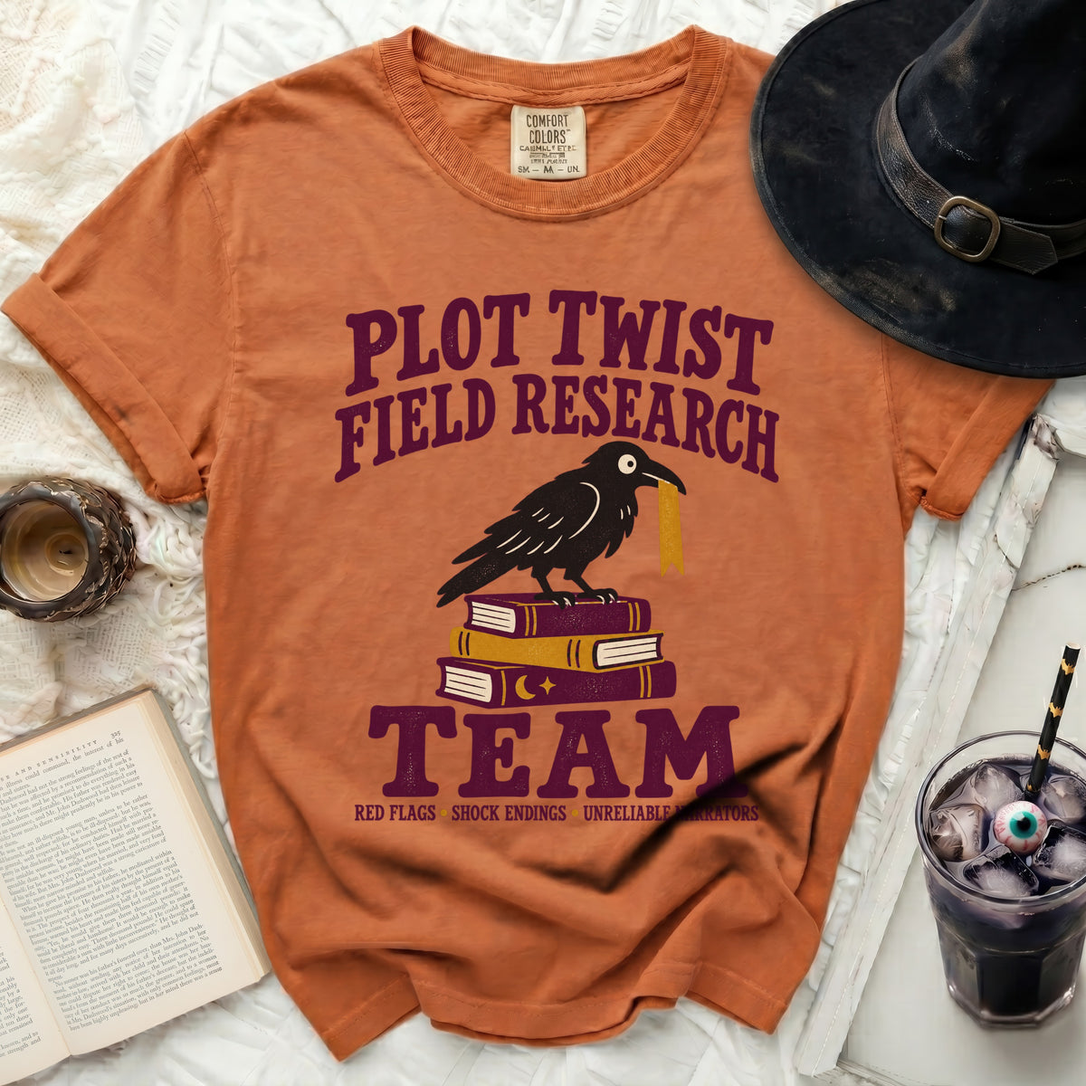 Orange t-shirt with "Plot Twist Field Research Team" text, crow on books.