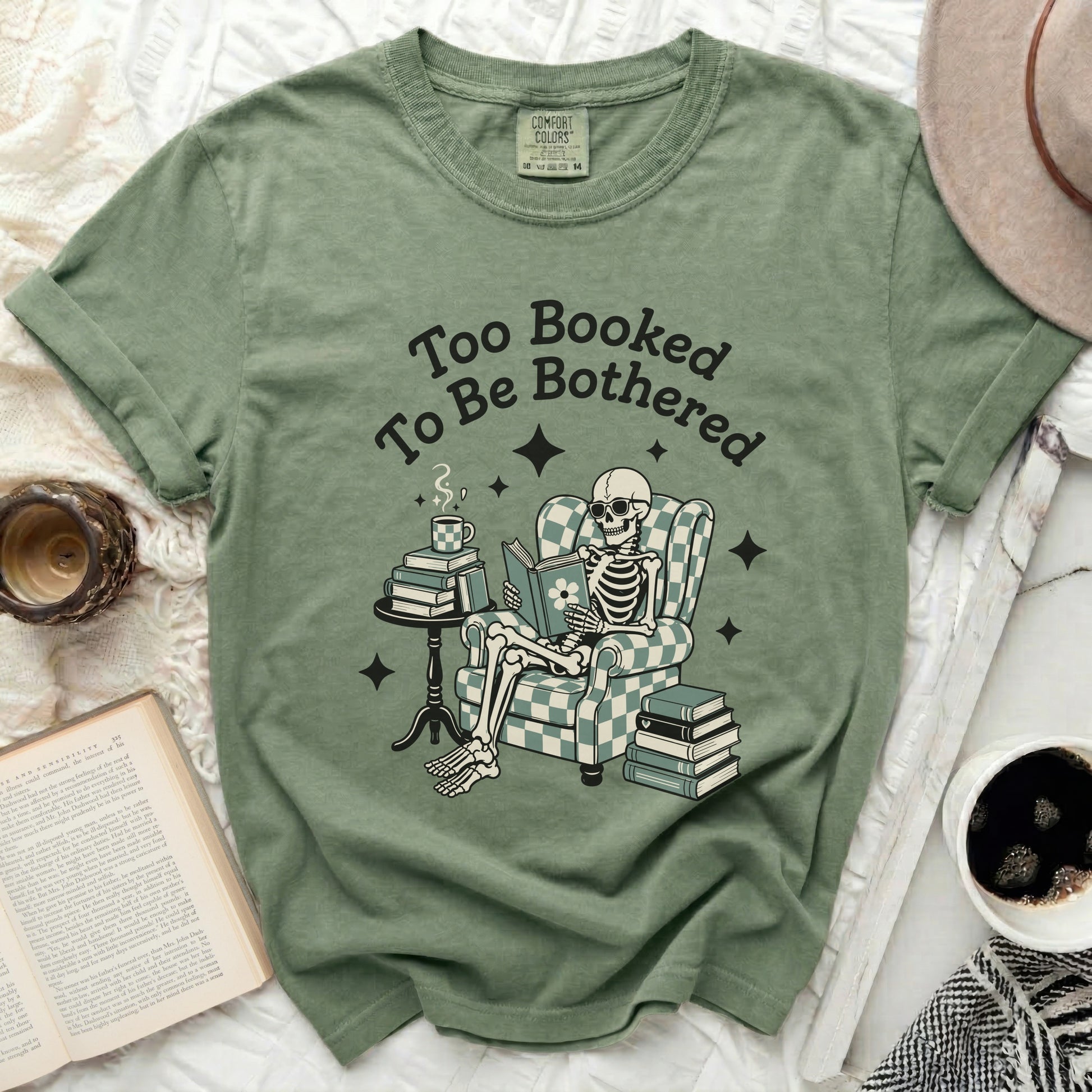Green t-shirt with skeleton reading on chair, text "Too Booked To Be Bothered"