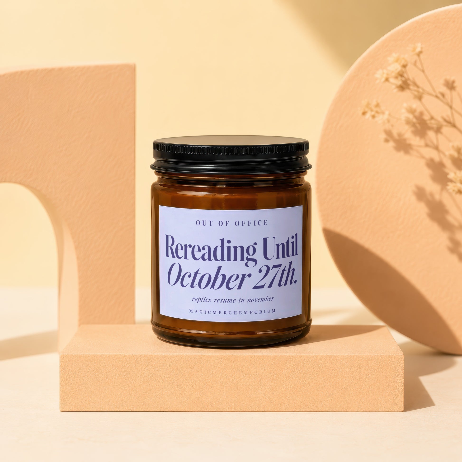 Amber glass candle jar with a black lid and a blue label reading "Rereading Until October 27th."