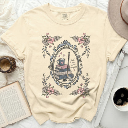 Cream t-shirt with framed stack of books, hockey stick, coffee cup, and floral design.