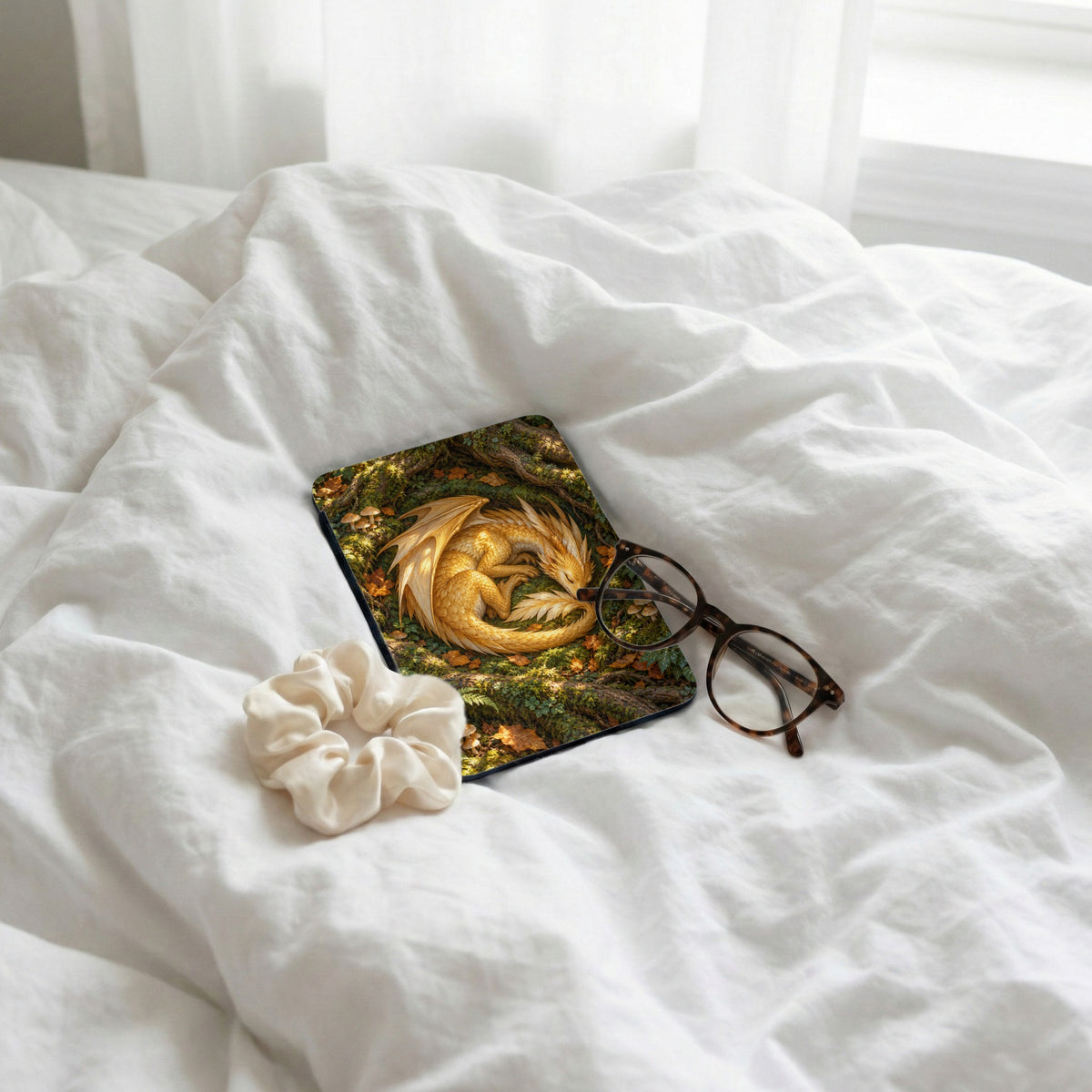 Golden dragon curled on forest floor, eyeglasses, and scrunchie on white sheets.