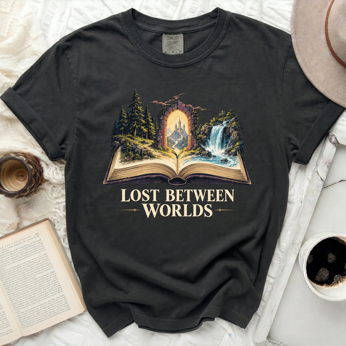 Dark t-shirt with an open book graphic depicting a castle through an archway and the text "Lost Between Worlds".