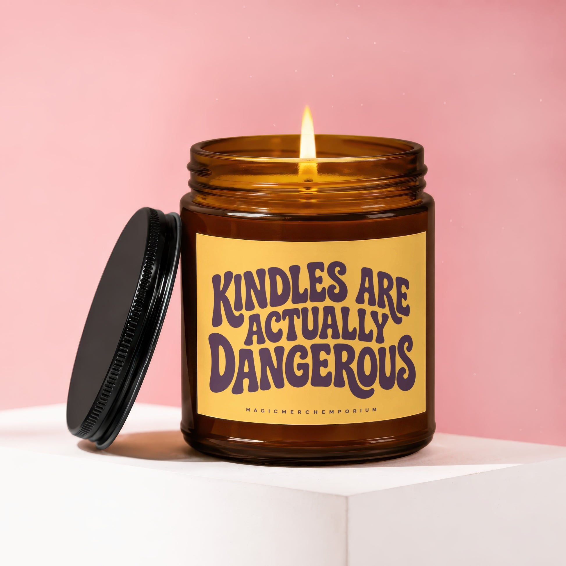 Amber candle with lit wick and black lid, reads "Kindles are actually dangerous."