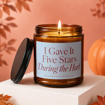 Lit amber glass candle with lid off, reading "I Gave It Five Stars During the Hurt".