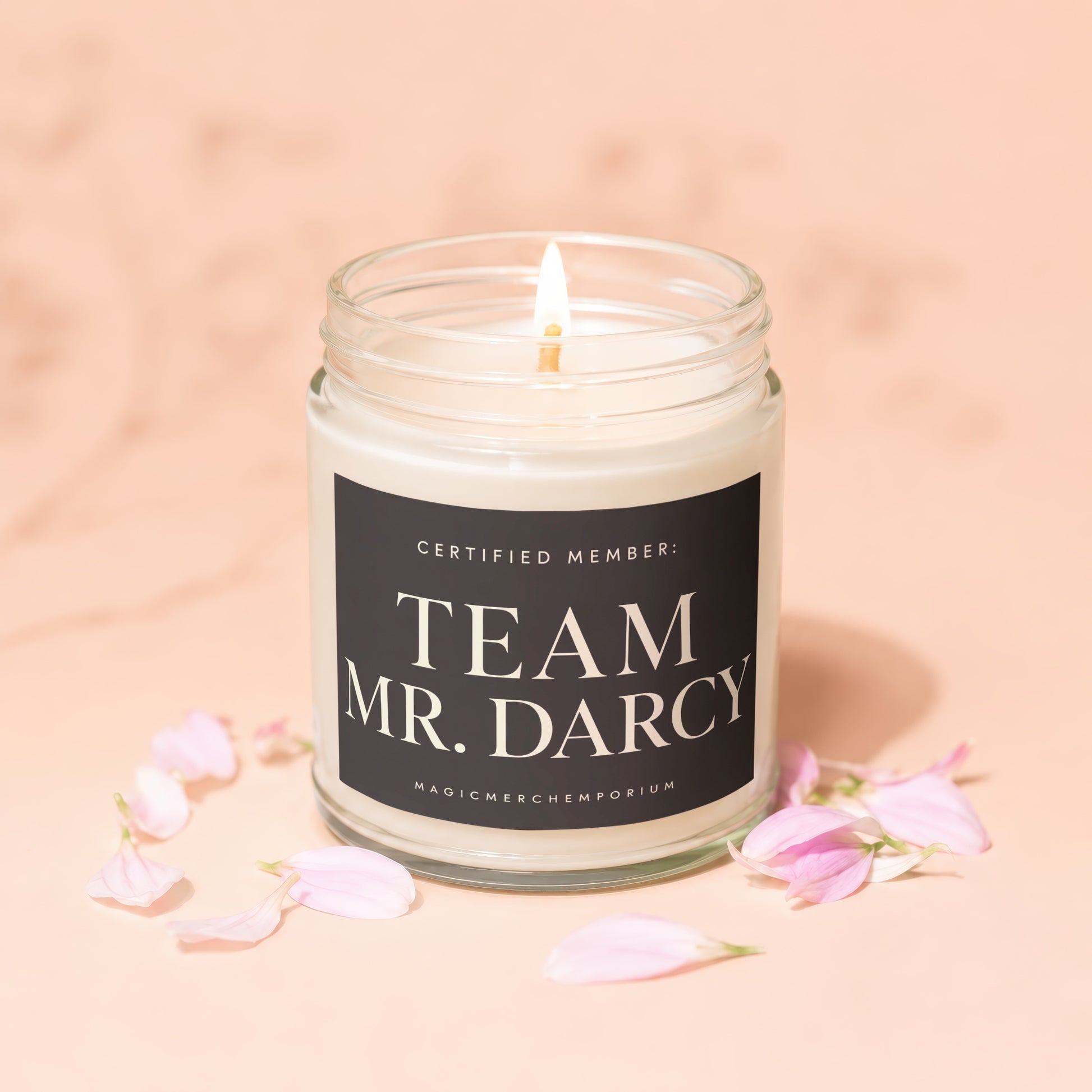 Lit candle in glass jar with "Team Mr. Darcy" label, surrounded by pink petals.