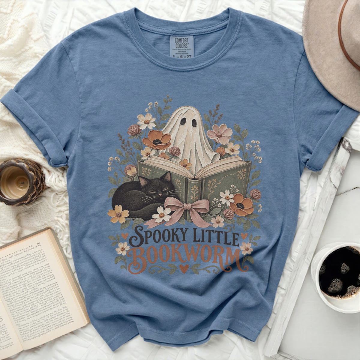 Spooky little bookworm graphic on blue t-shirt with ghost, cat, and floral design.