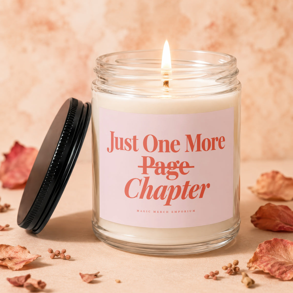 Glass jar candle with lit wick and pink label reading "Just One More Page Chapter".