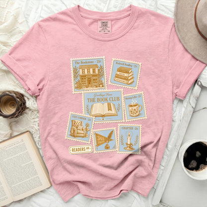 Pink t-shirt with stamps featuring books, coffee, and a quill.