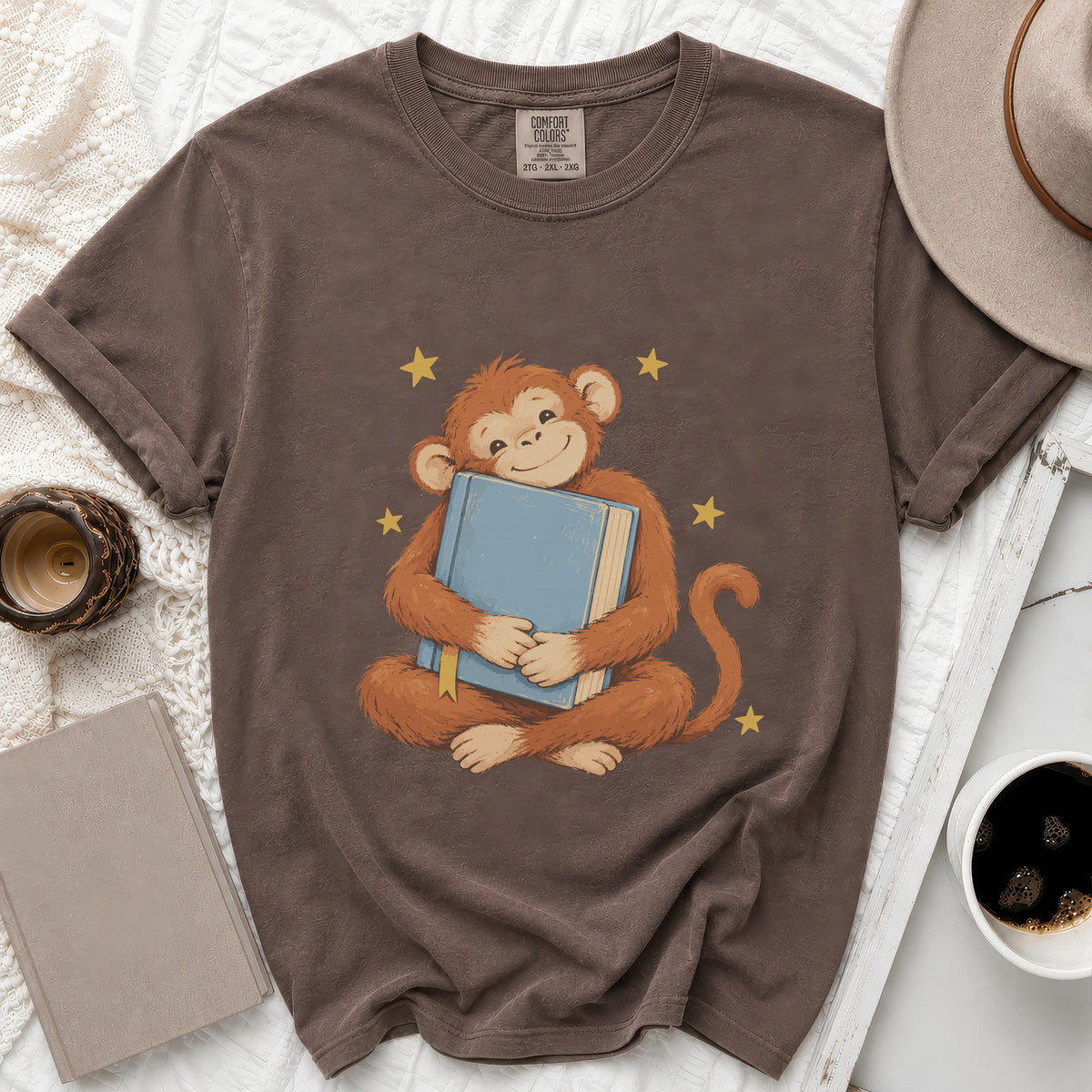 Brown t-shirt with a monkey hugging a blue book and yellow stars.