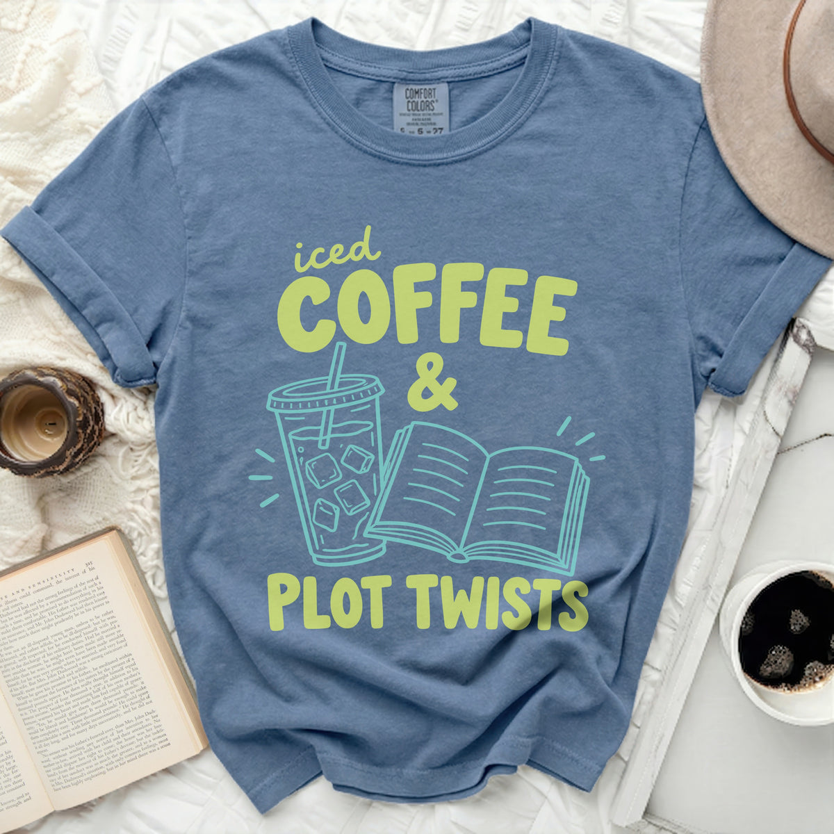 Blue t-shirt with text "iced COFFEE & PLOT TWISTS" and graphic of iced drink and book.