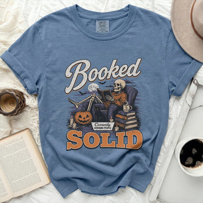 Blue t-shirt with skeleton reading in armchair, "Booked" and "SOLID" text.