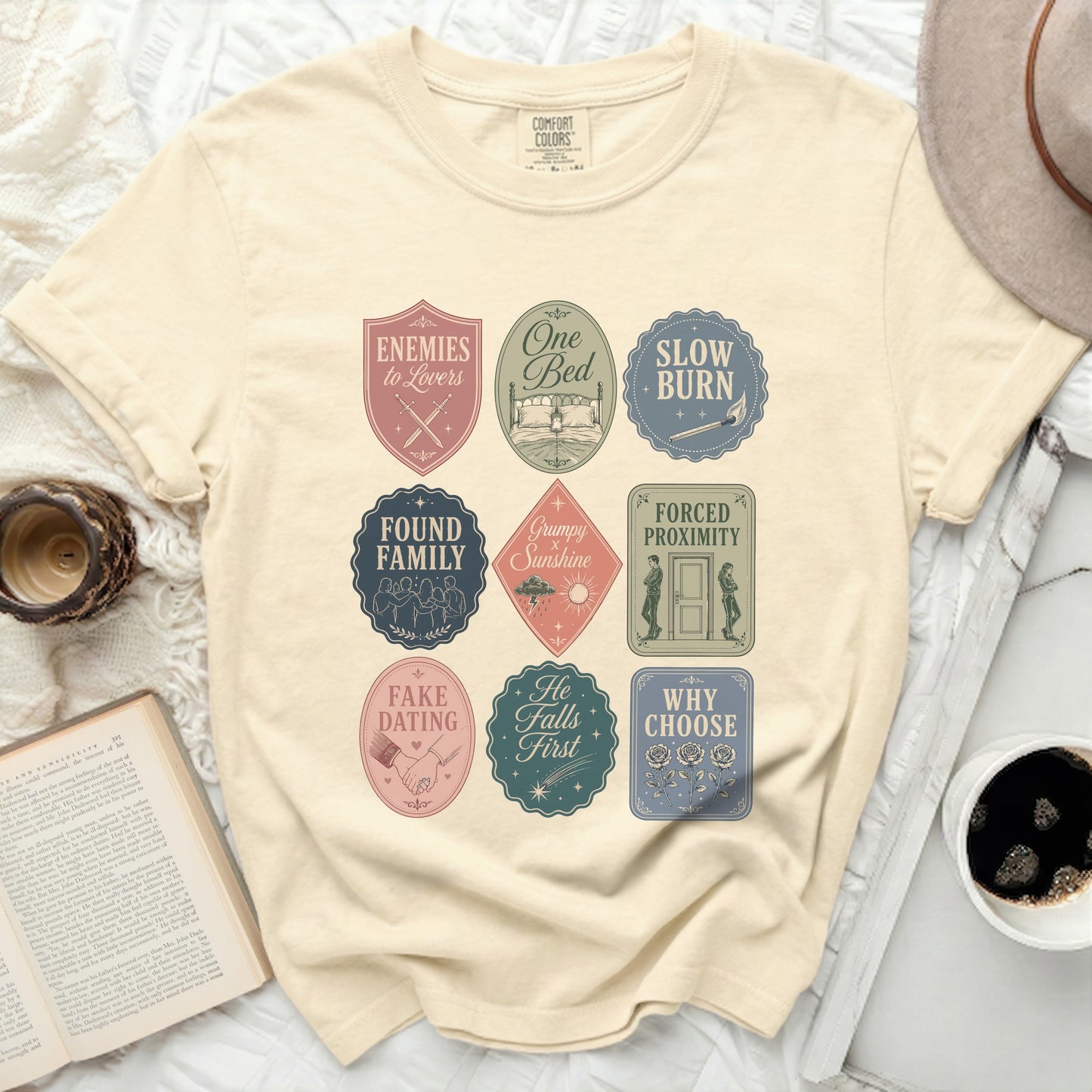 Cream t-shirt with nine circular book trope badges in pastel colors.