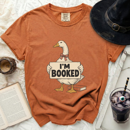 Orange t-shirt with a duck graphic holding an "I'M BOOKED" sign.