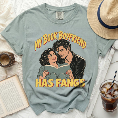 Light blue t-shirt with comic style art of a couple reading and the text "MY BOOK BOYFRIEND HAS FANGS".