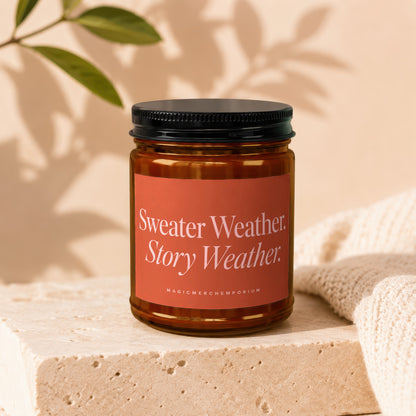 Candle with "Sweater Weather Story Weather" label on a textured stone block near knitted fabric.