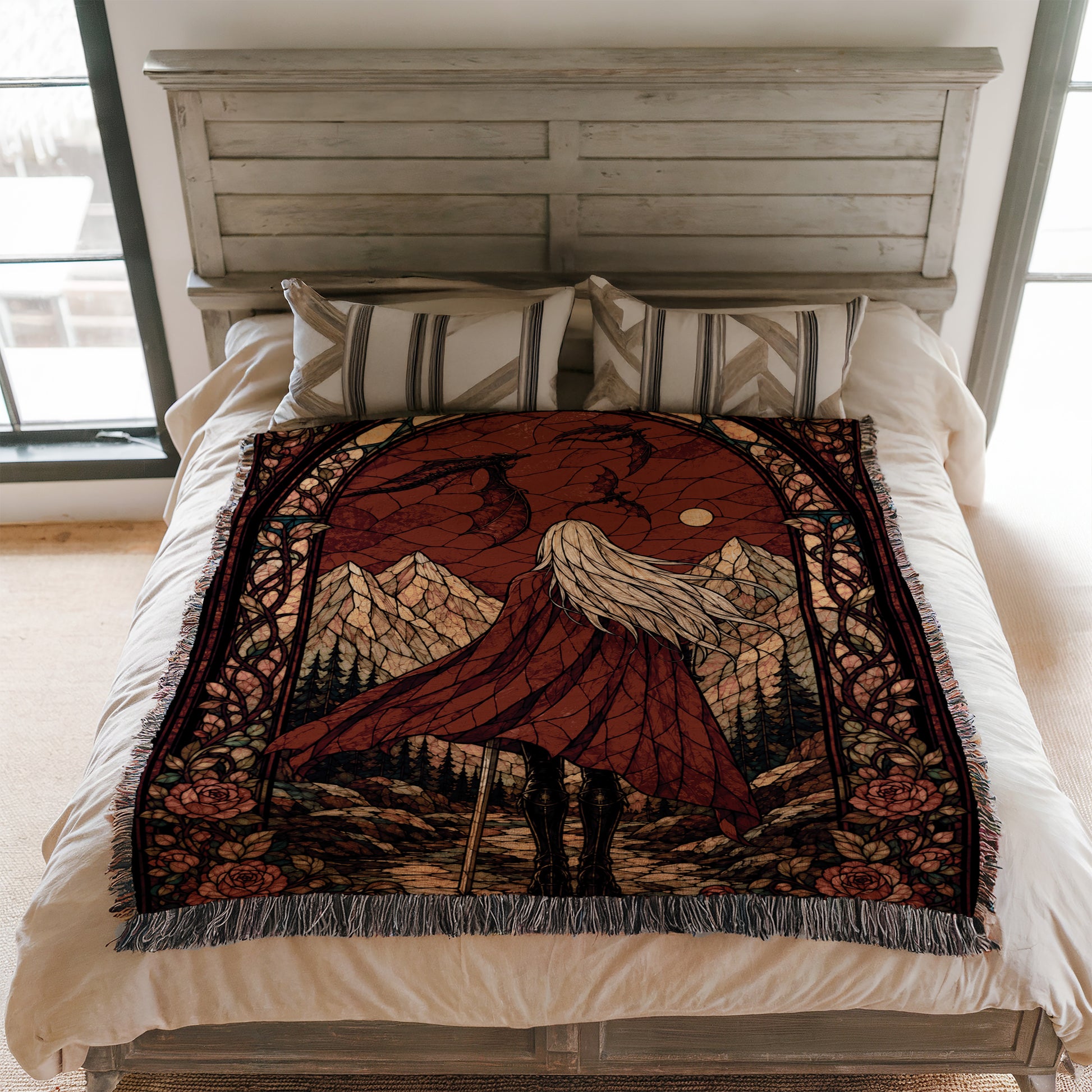 a bed with a large, colorful, and intricate blanket on it. The blanket features a scene of a woman with long hair, wearing a red cape, standing in front of a mountain landscape. The blanket is placed on a white bedspread, and there are pillows on the bed.