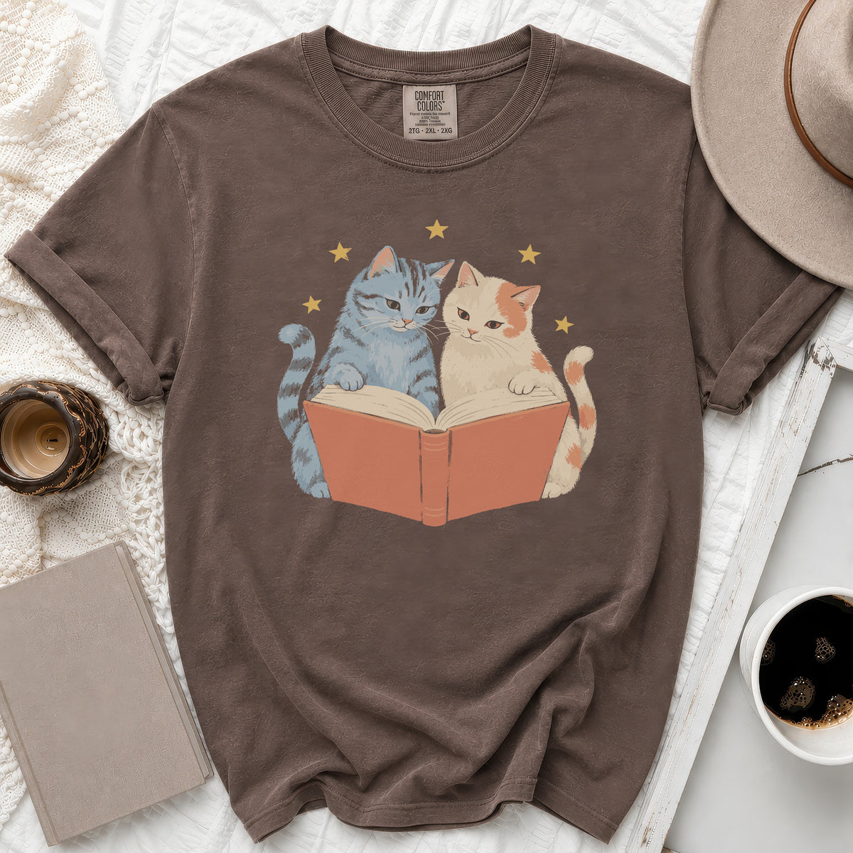 Brown t-shirt with a graphic of two cats reading a book under stars.