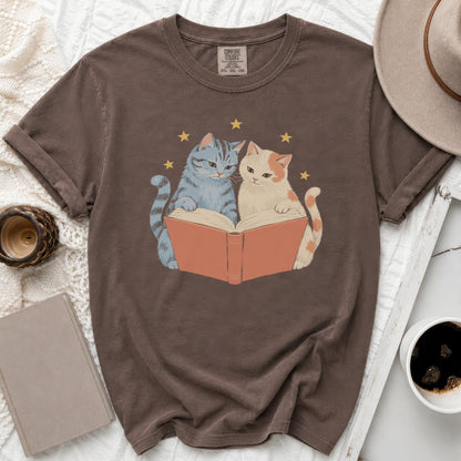 Brown t-shirt with a graphic of two cats reading a book under stars.