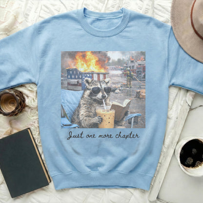 Light blue sweatshirt with raccoon wearing sunglasses reading and drinking coffee.