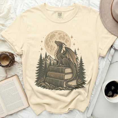Dragon on books in front of moon and pine trees graphic on cream t-shirt.