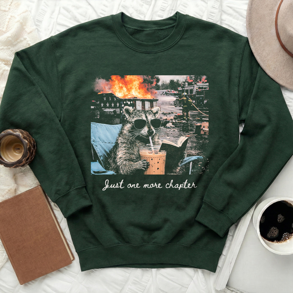 Raccoon wearing sunglasses drinks iced coffee while reading next to a burning building.