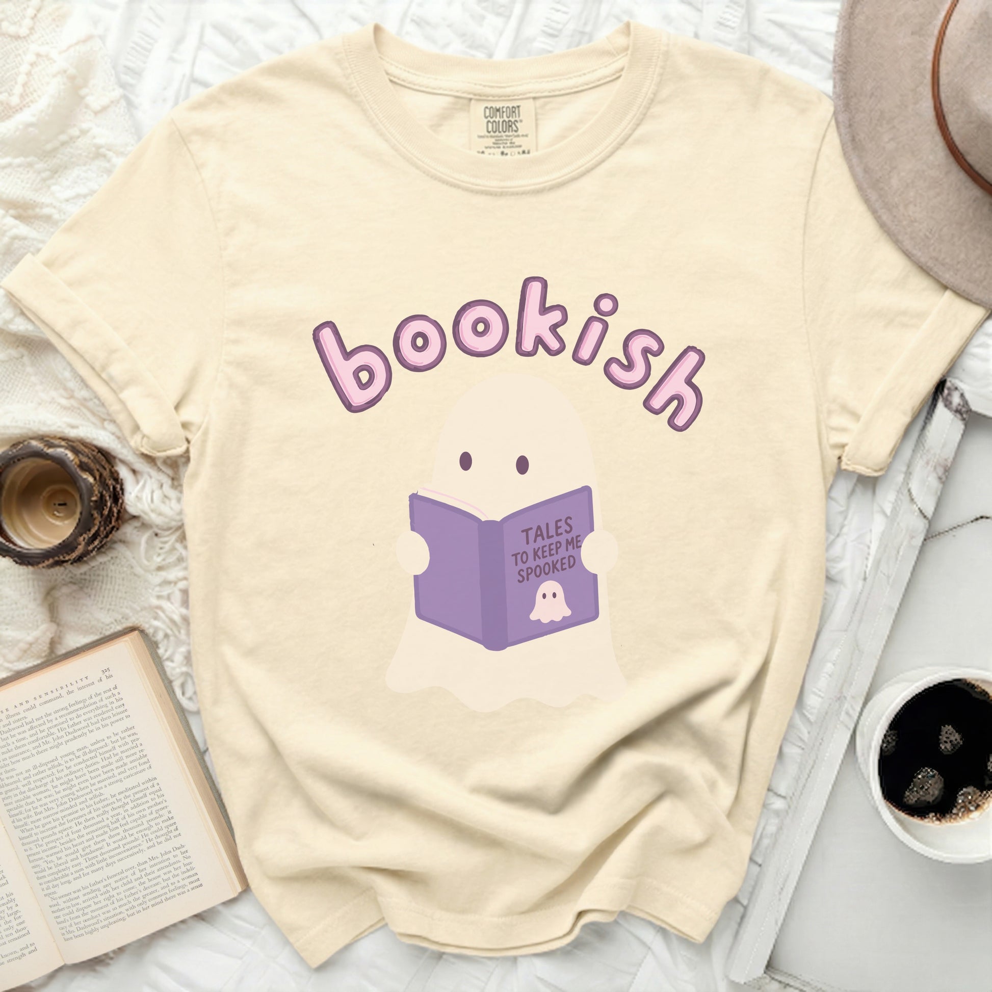 Cream t-shirt with a ghost reading a book titled "Tales to Keep Me Spooked."