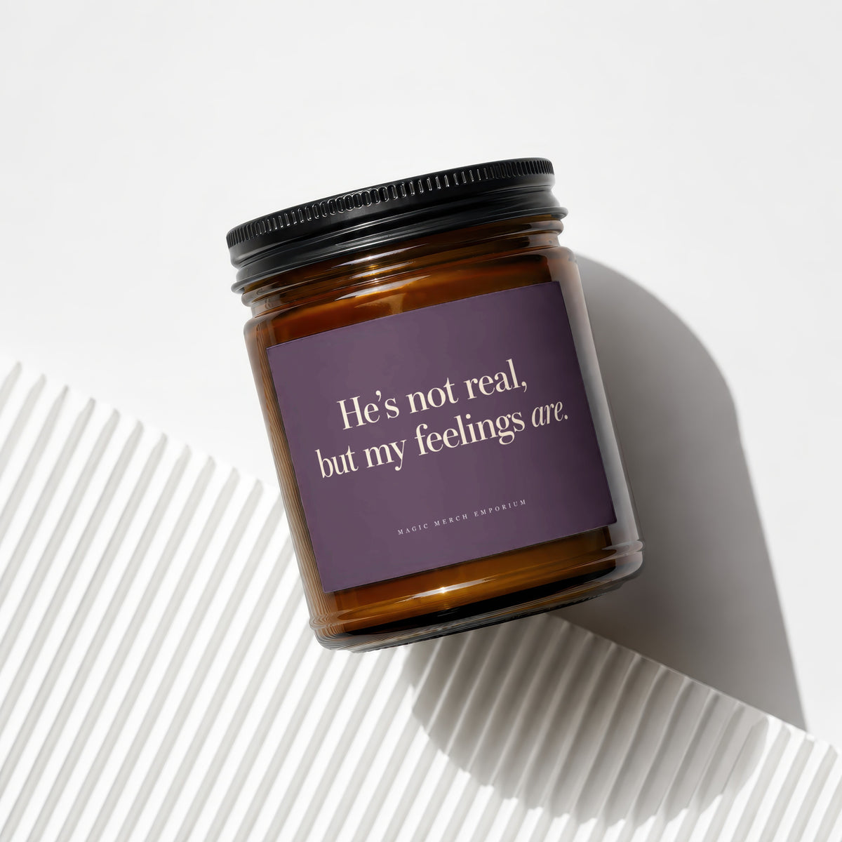 Amber glass candle with purple label reading "He's not real, but my feelings are."