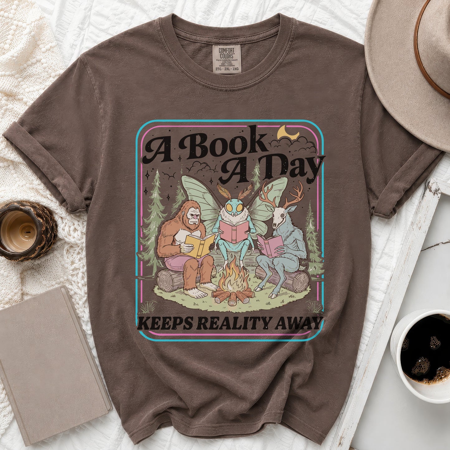 Bigfoot, moth, and deer reading books around a campfire with text "A Book A Day Keeps Reality Away."