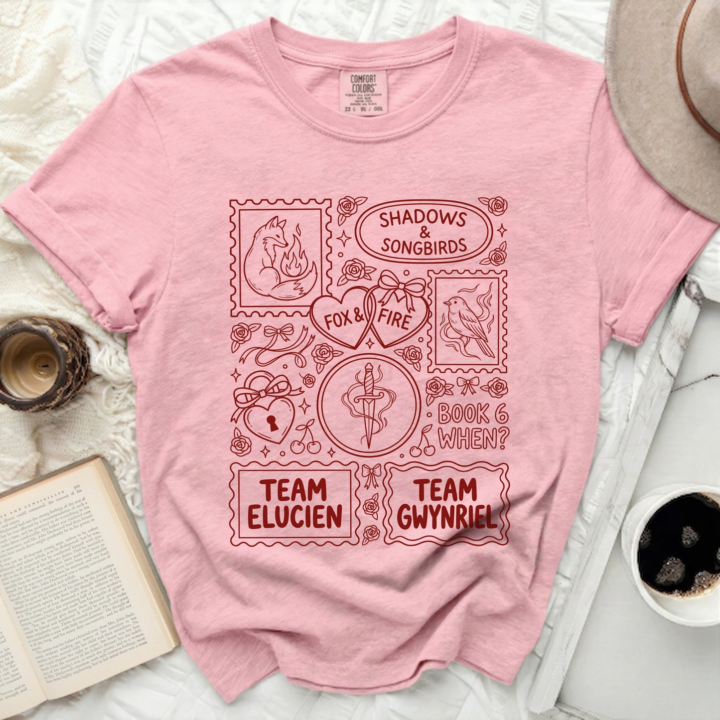 Pink t-shirt with red stamp-like graphics: fox, bird, dagger, hearts, text.