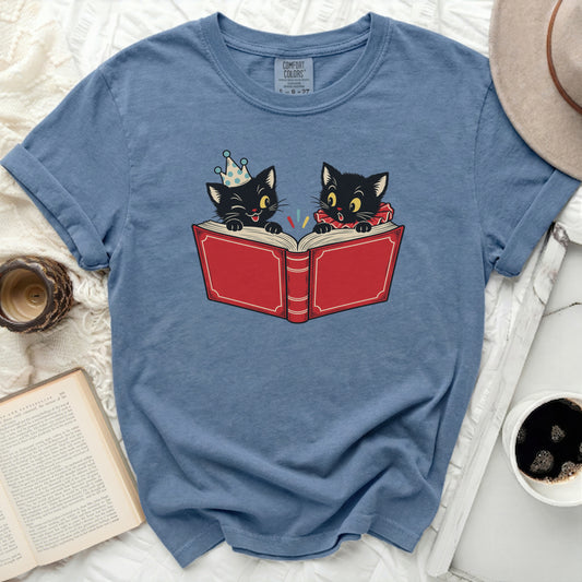Blue t-shirt featuring two illustrated black cats reading a large red book.
