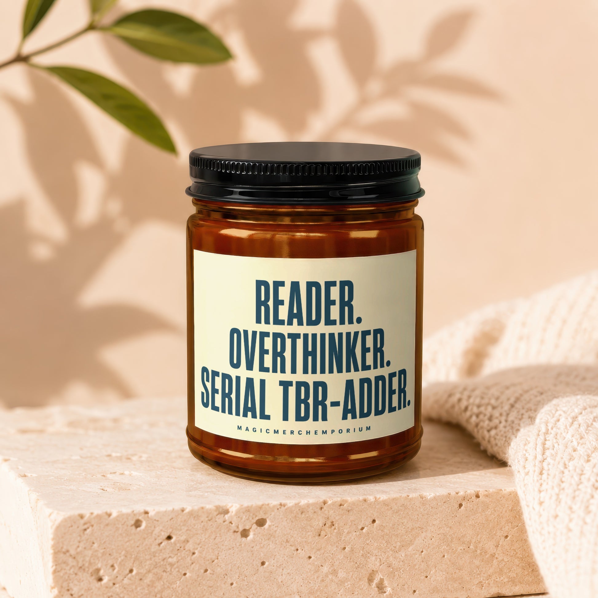 Amber jar candle with black lid, text: "READER. OVERTHINKER. SERIAL TBR-ADDER."