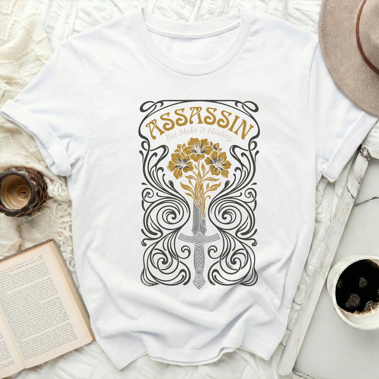 White t-shirt with an ornate floral and sword design and "ASSASSIN But Make It Healing" text.
