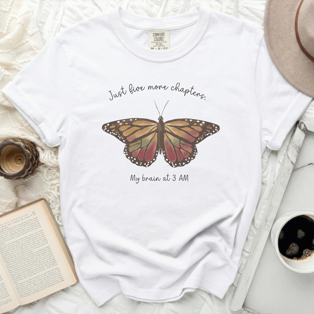 White t-shirt with a butterfly graphic and text "Just five more chapters. My brain at 3 AM."