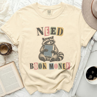 T-shirt with raccoon holding book and text "NEED BOOK MONEY".