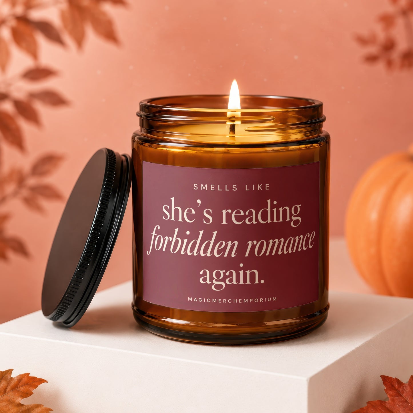 Amber candle with a lit wick and a burgundy label reading "she's reading forbidden romance again."