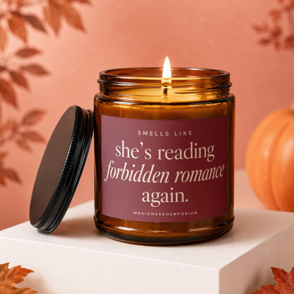 Amber candle with a lit wick and a burgundy label reading "she's reading forbidden romance again."