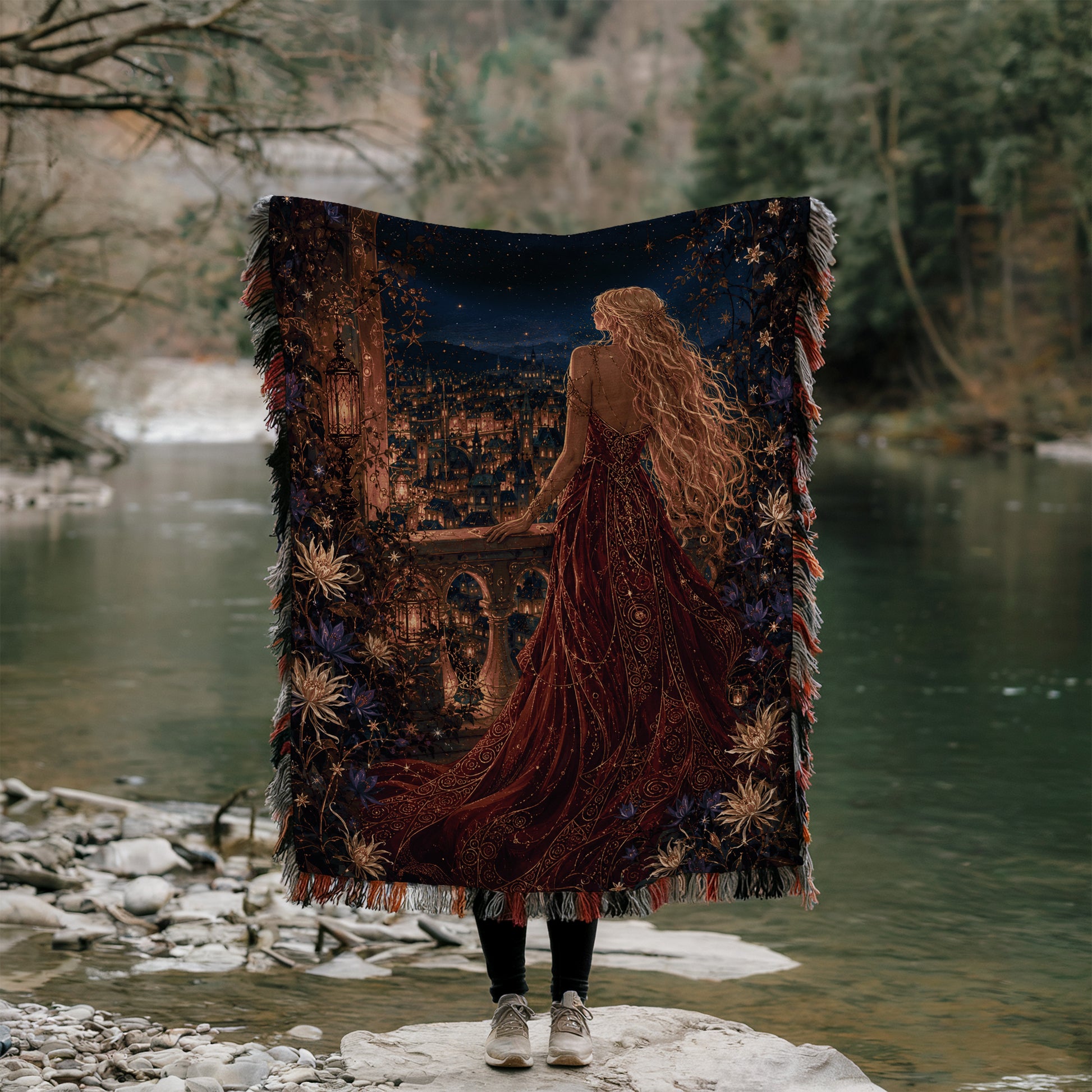 A person stands on a rock, holding a large tapestry that depicts a woman with long, flowing hair and a red dress, gazing out at a river or lake.