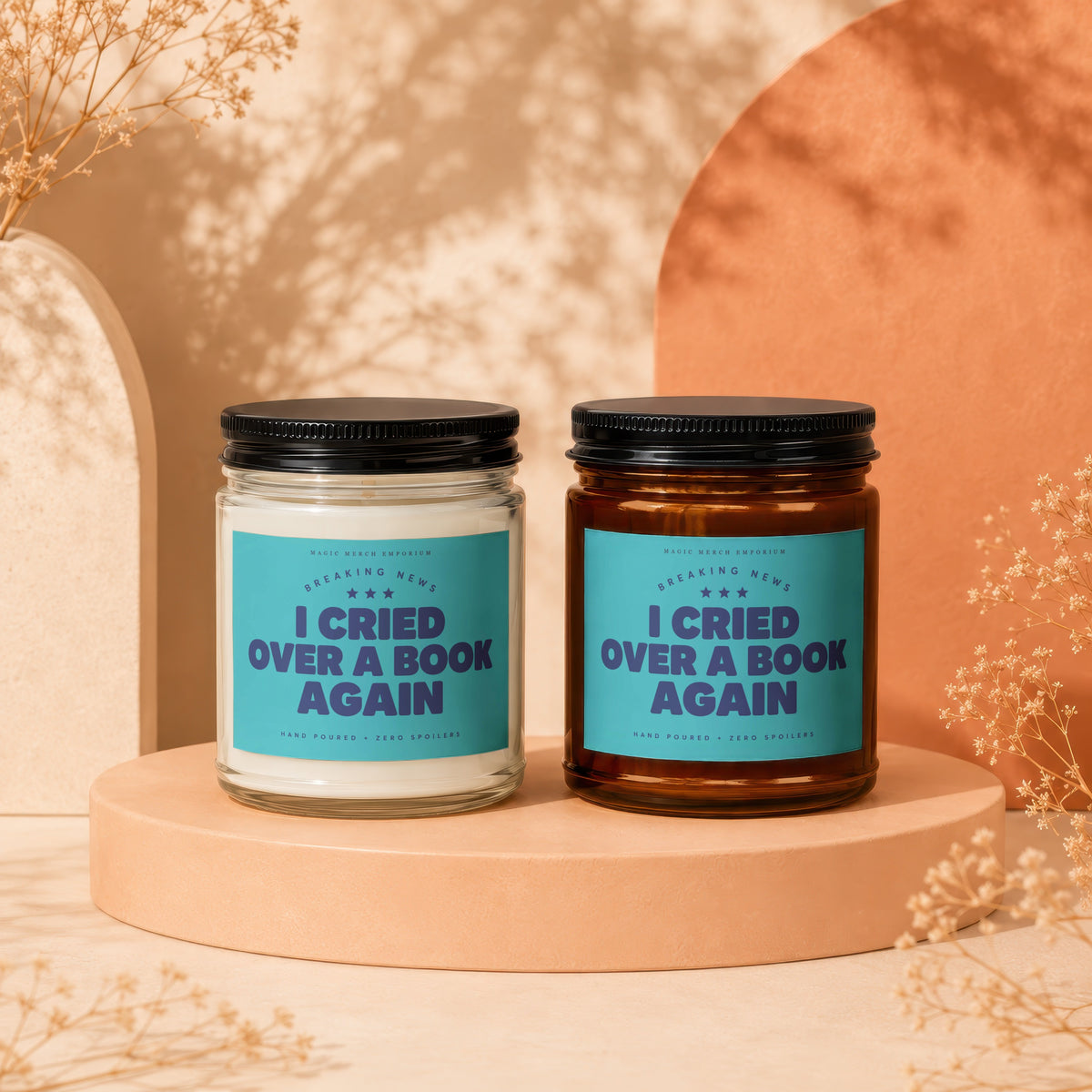 Two glass candles with teal labels reading "I Cried Over a Book Again" sit on a beige pedestal.
