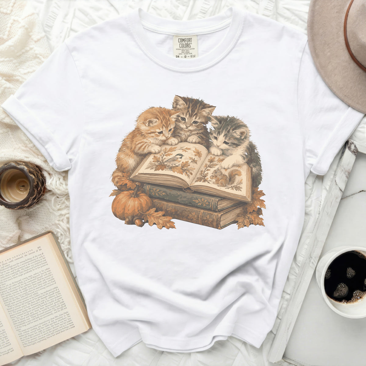 Three kittens read a book with autumn leaves, pumpkins, and acorns.