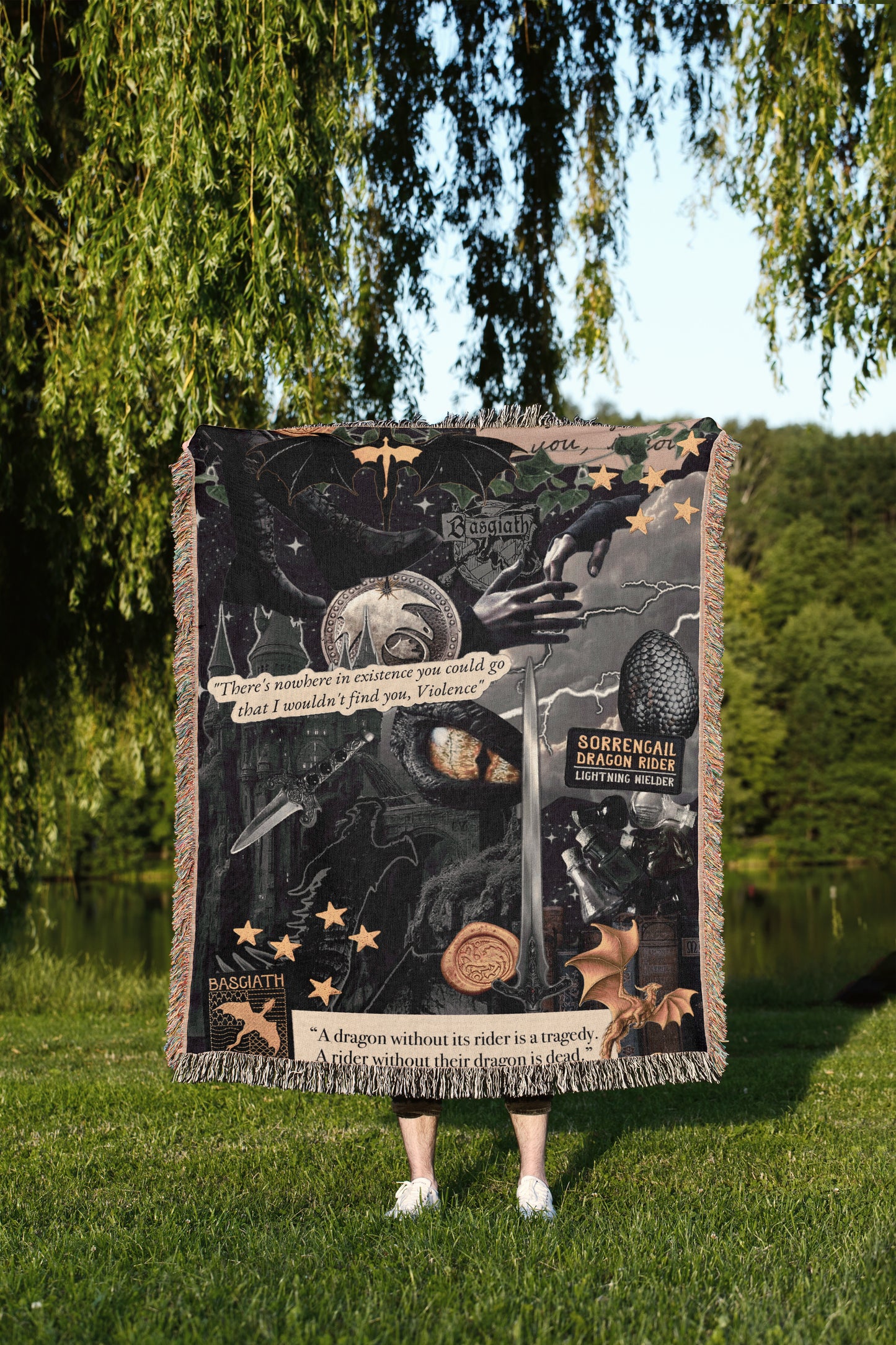 A person is standing in a grassy area, holding a large, colorful blanket or quilt with various images and text printed on it.