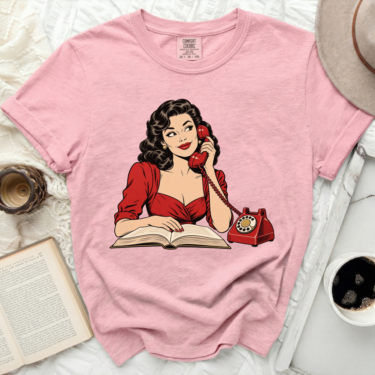 Pink t-shirt with retro illustration of woman on phone reading a book.