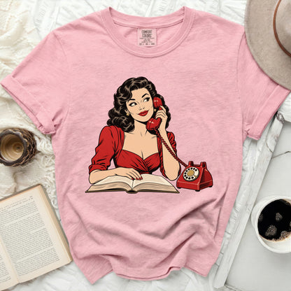 Pink t-shirt with retro illustration of woman on phone reading a book.