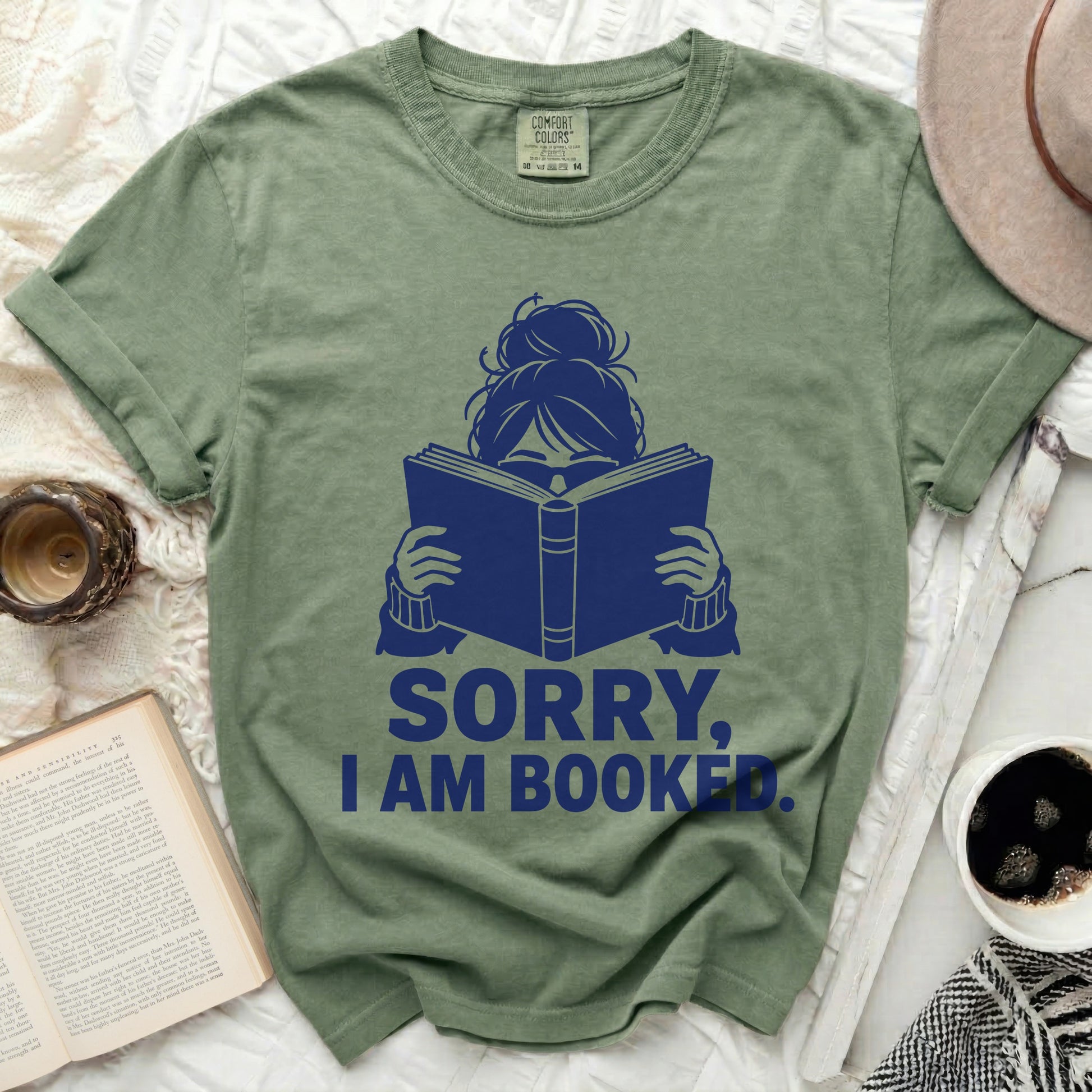 Olive t-shirt with navy graphic of a person reading and the text "SORRY, I AM BOOKED."