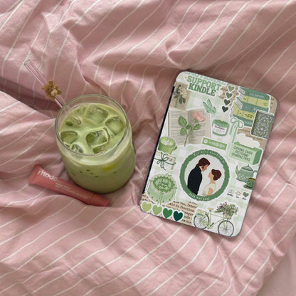 Green iced matcha drink and a sticker-covered Kindle on a pink striped blanket.