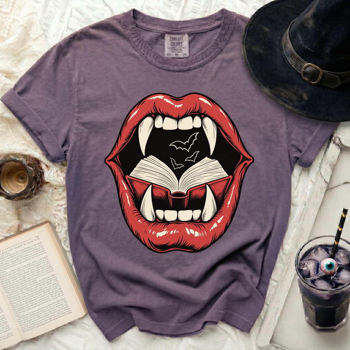 Purple t-shirt with a vampire mouth graphic biting an open book with bats.