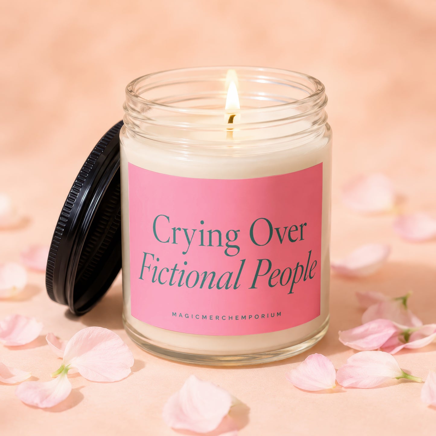 Glass candle with lit wick and pink label reading "Crying Over Fictional People"