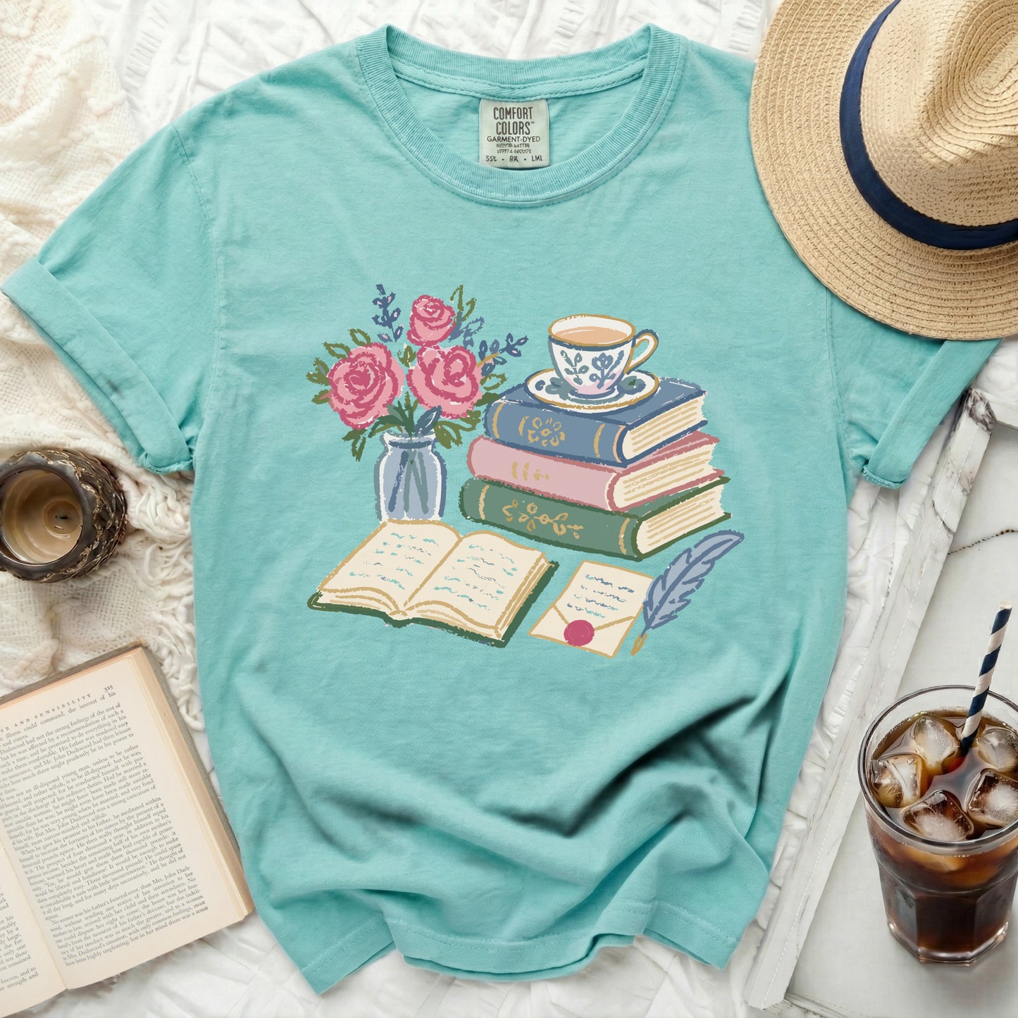 Teal t-shirt with a graphic of books, flowers, teacup, and feather quill.